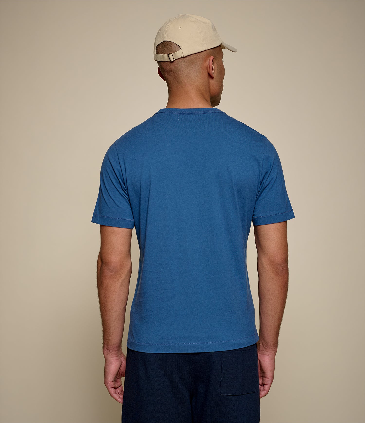 Man wearing an indigo blue t-shirt and beige cap on a beige background