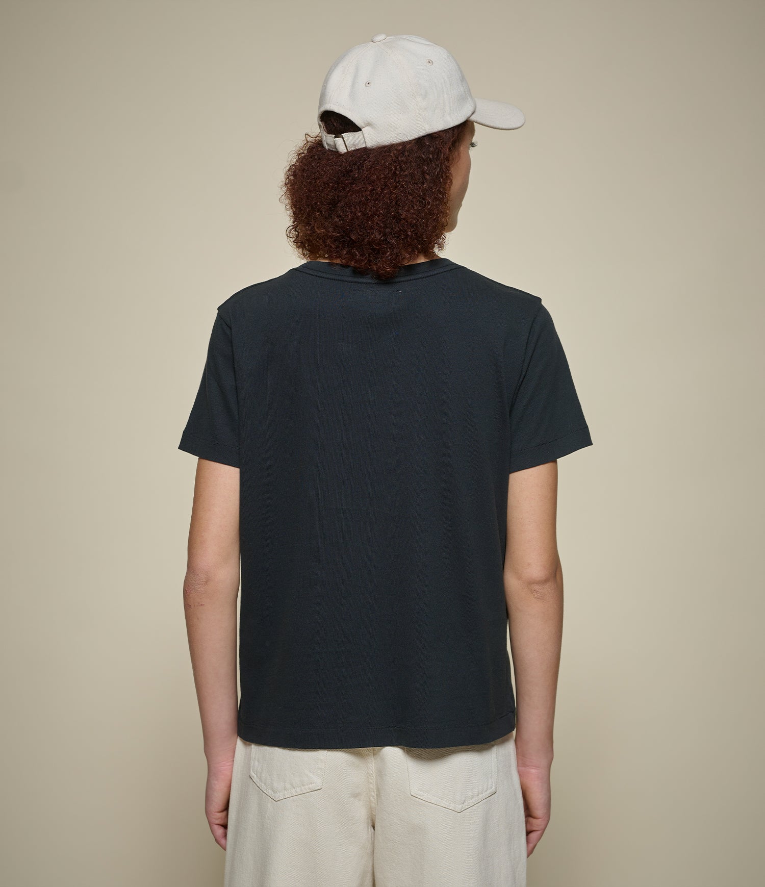 Person wearing a black t-shirt and beige cap on a plain background