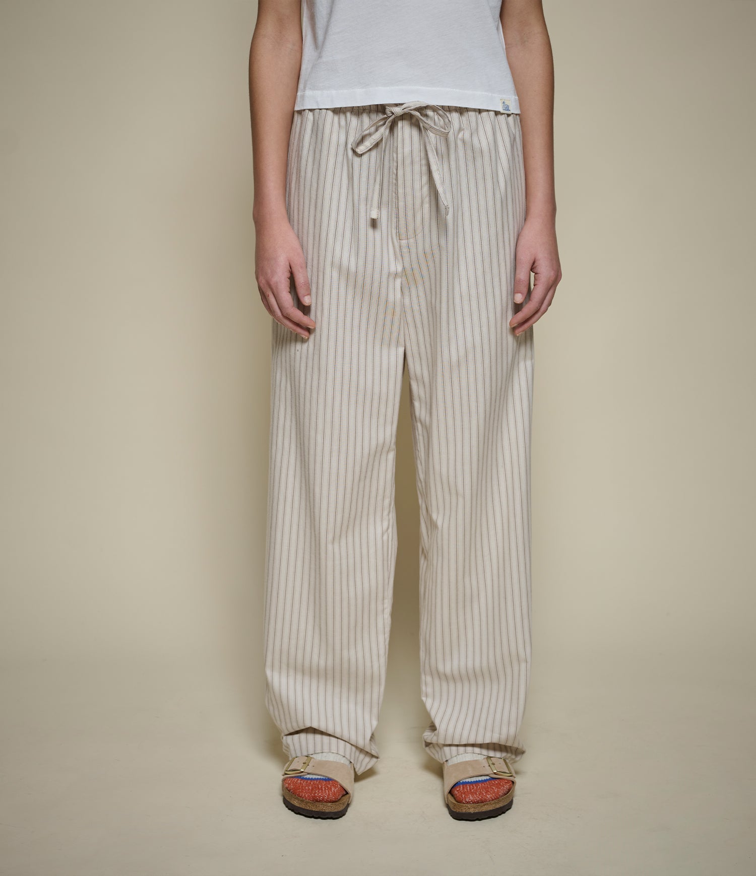 A person wearing loose, wide-leg striped pants with a drawstring waist, shown from the shoulders down against a plain beige studio background.