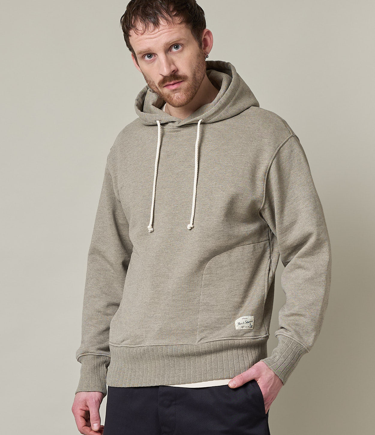 A male model wearing a gray heavyweight rugged fleece cotton hoodie with a hood and drawstrings.