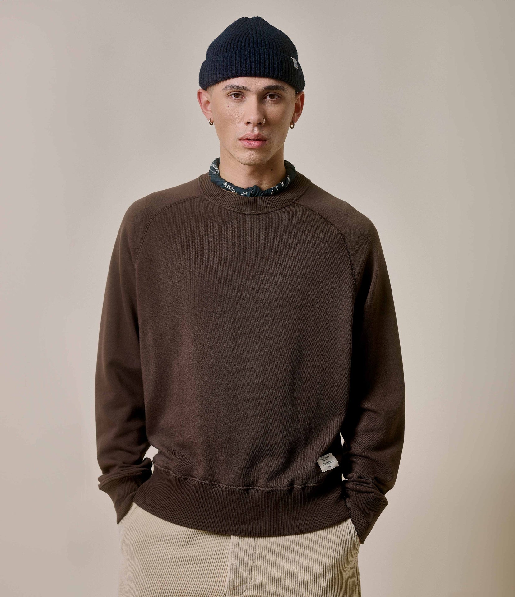 Person wearing a brown sweatshirt and black beanie on a plain background