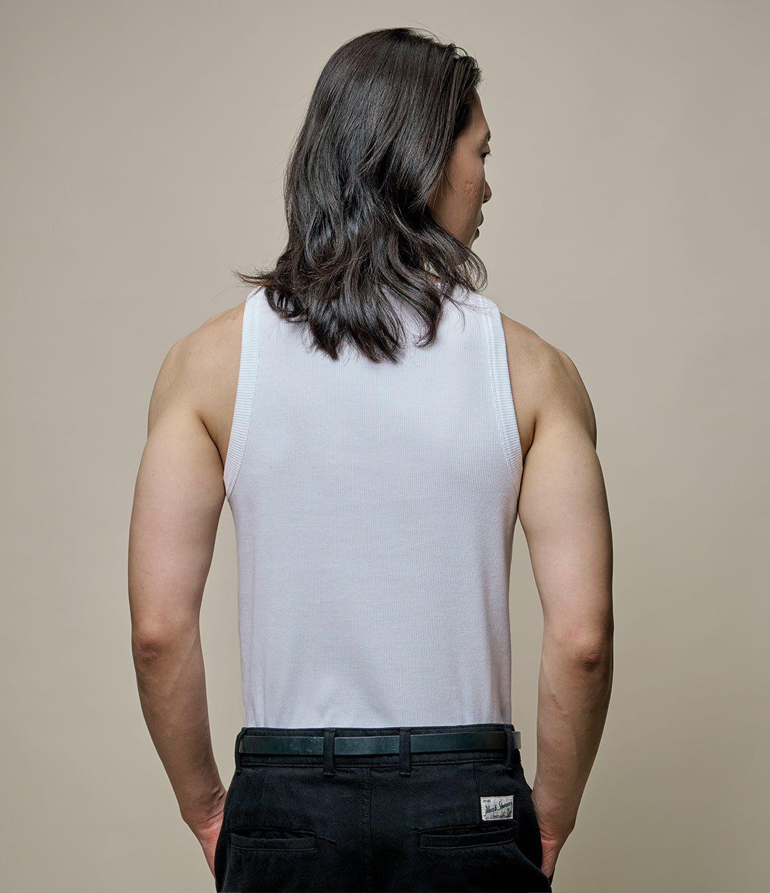 Person wearing a white tank top and black pants against a beige background