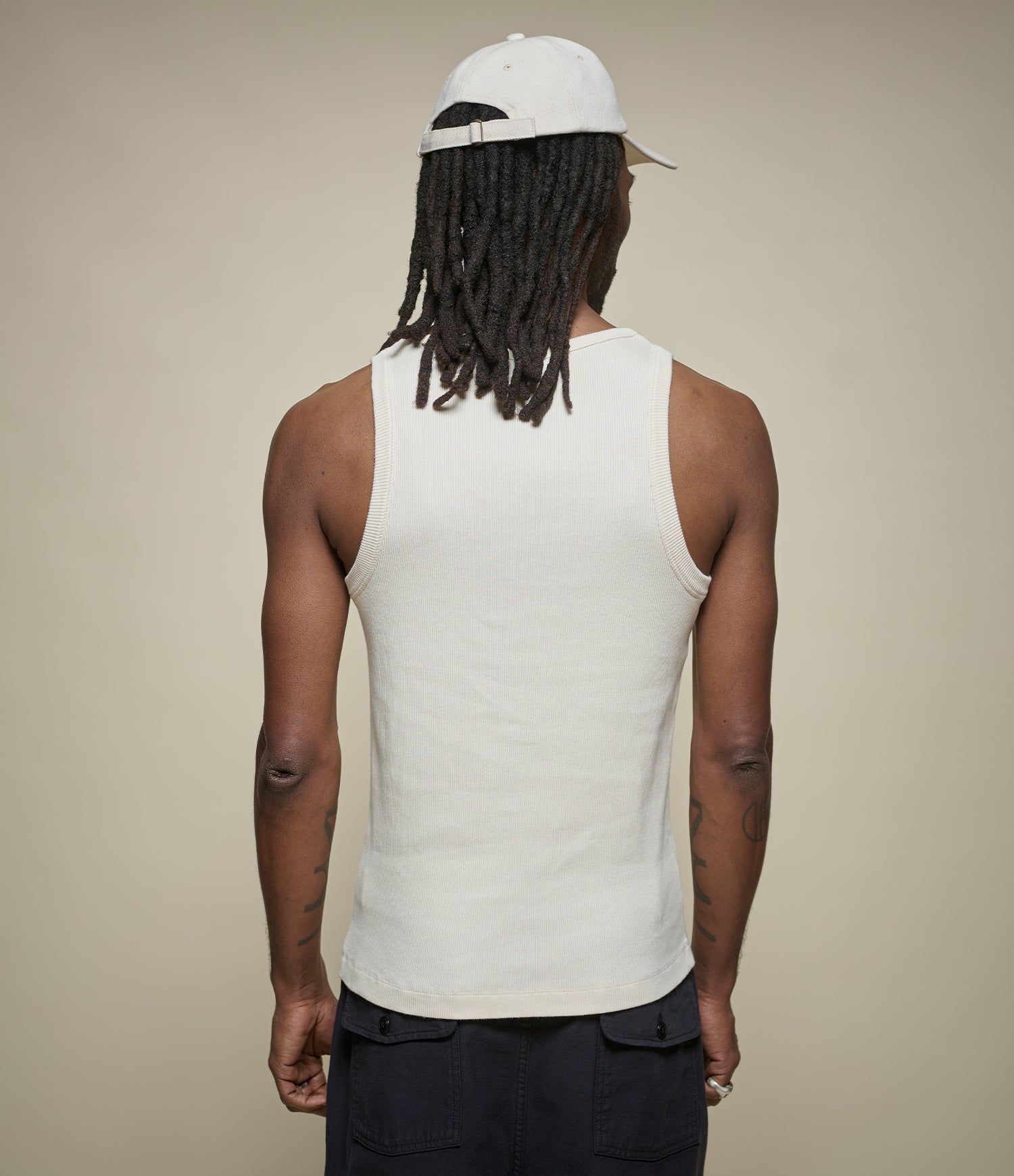 Person wearing a beige tank top and black pants with a beige background