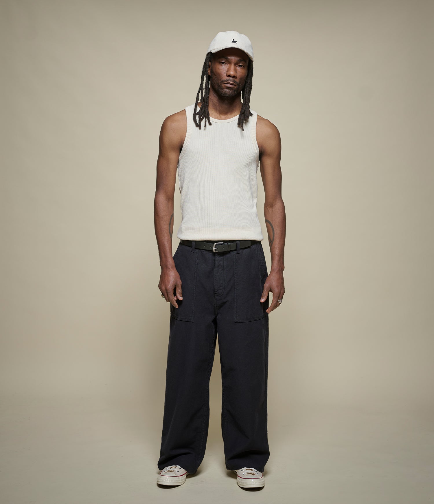 Person wearing a beige tank top and black pants on a plain background