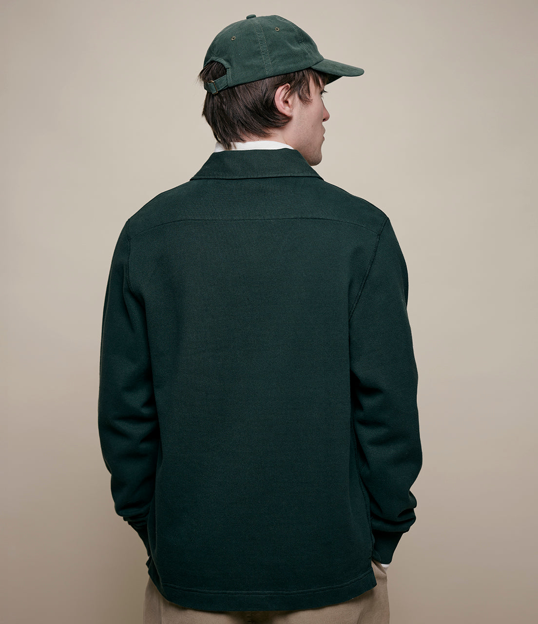 Person wearing a dark green rugby shirt and cap on a beige background