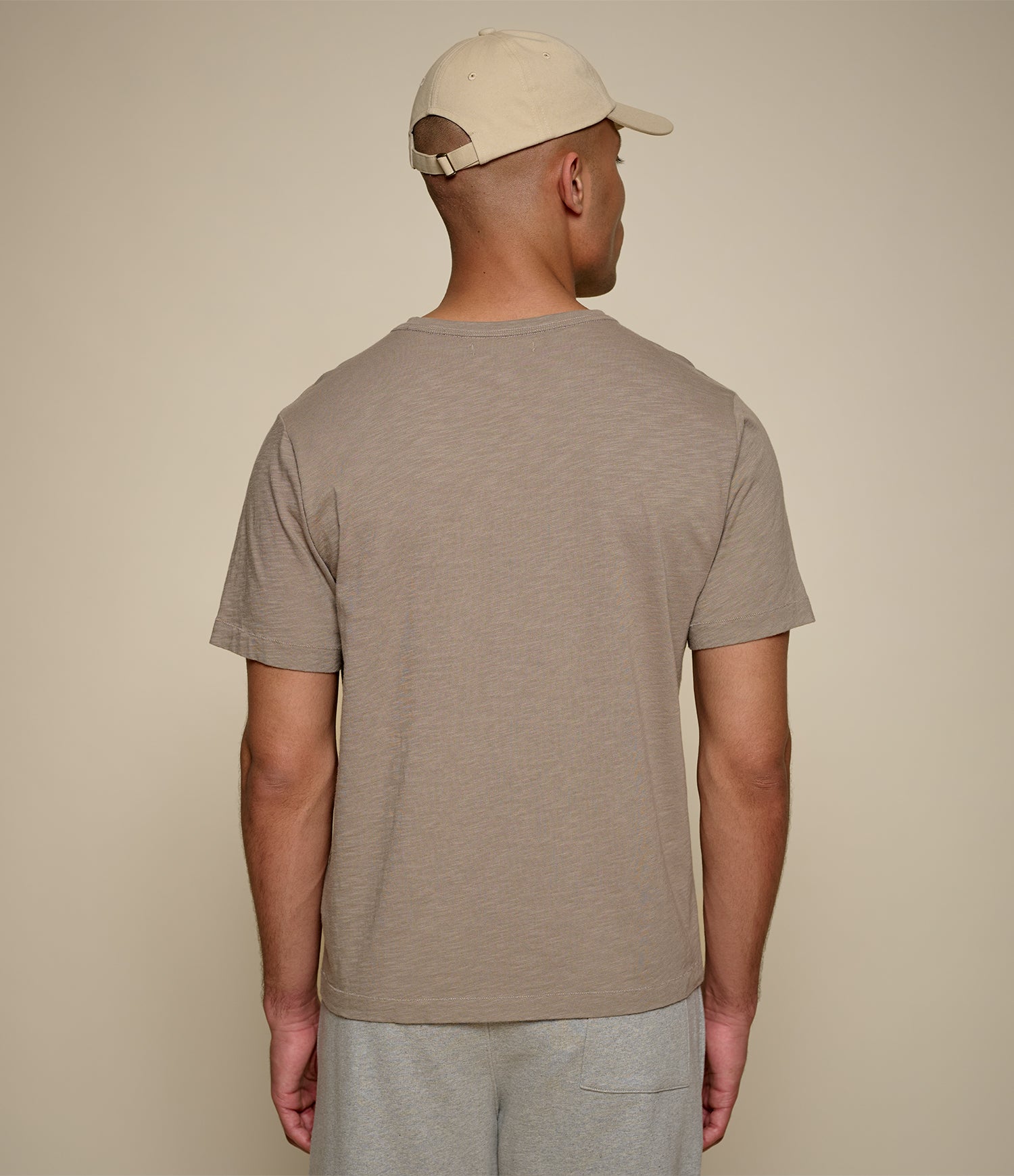Man wearing a brown t-shirt and cap against a beige background