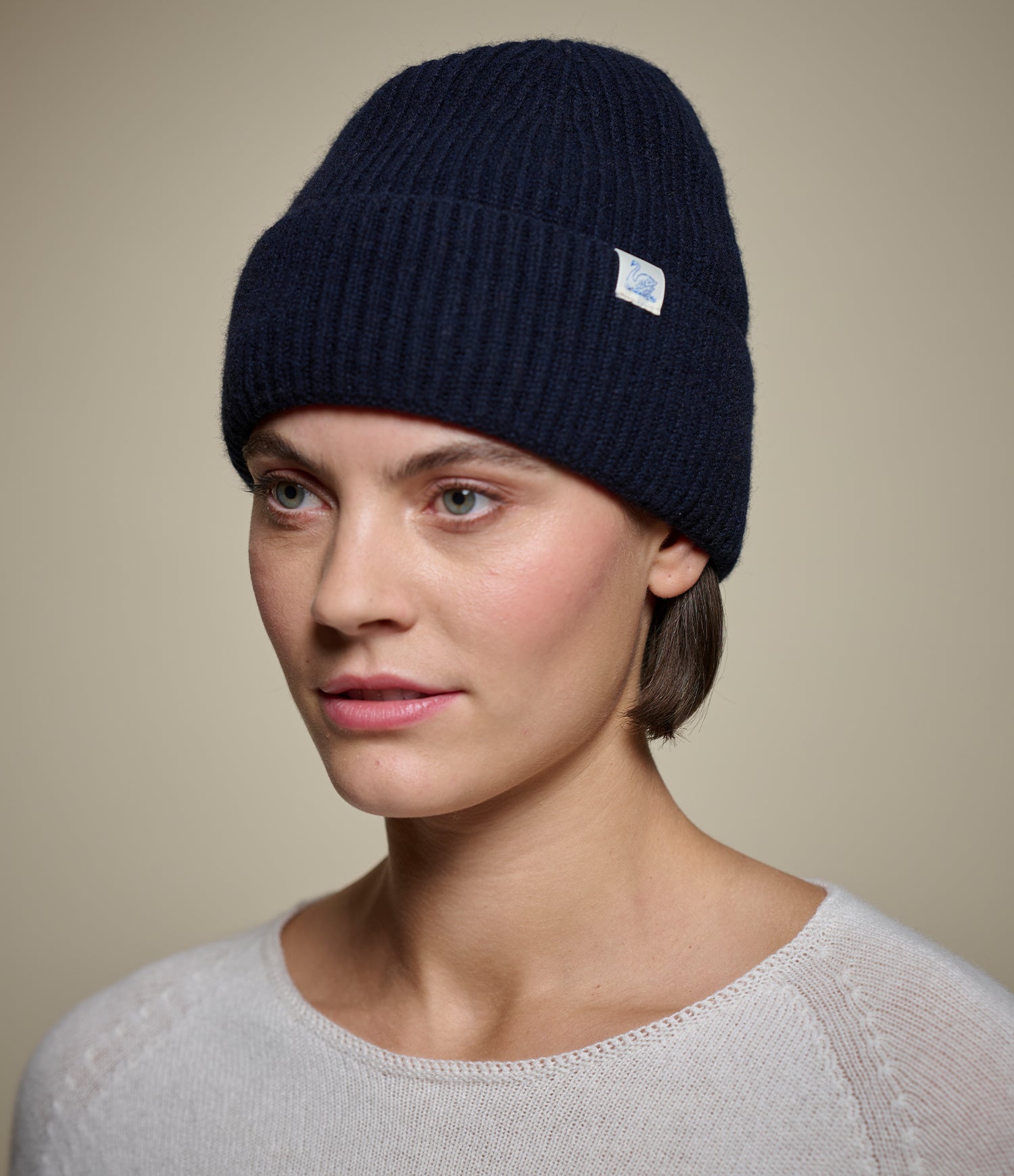 Person wearing a navy blue beanie with a logo on a beige background