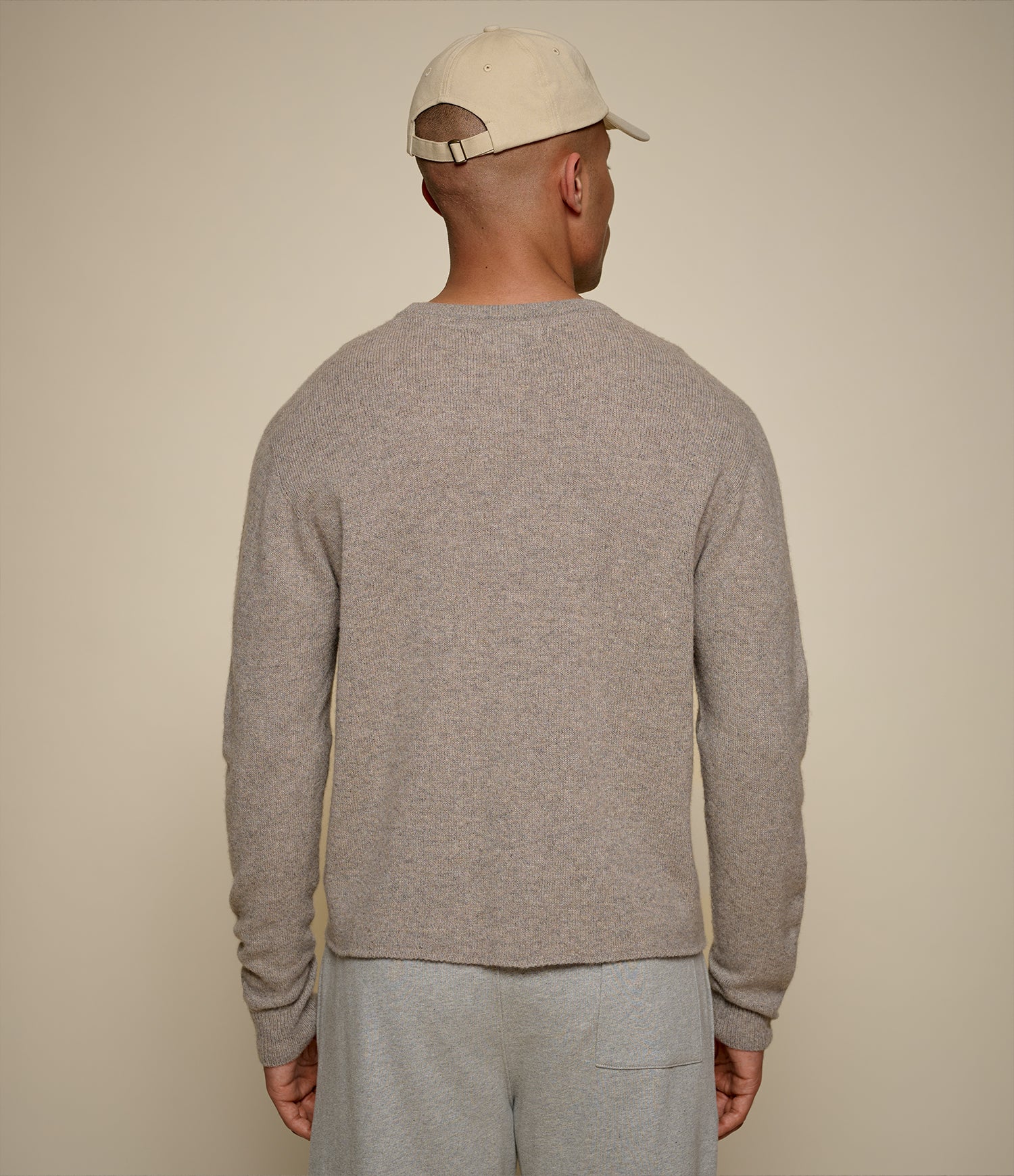 Man wearing a gray sweater and beige cap against a beige background