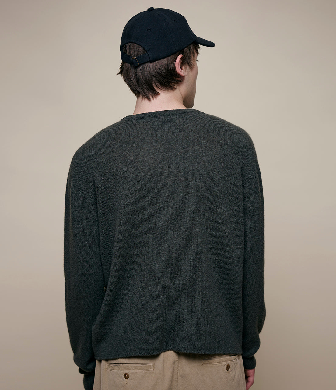 Person wearing a dark green sweater and black cap on a beige background