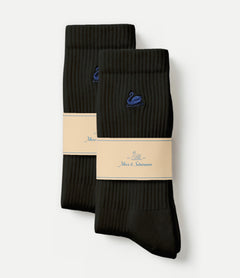 Two pairs of black ribbed crew socks with a blue swan logo and a beige paper band, displayed on a light gray background.