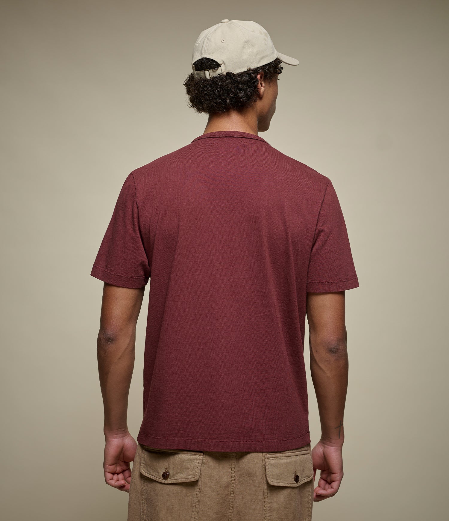Man wearing a maroon crew neck t-shirt and beige cap on a plain background