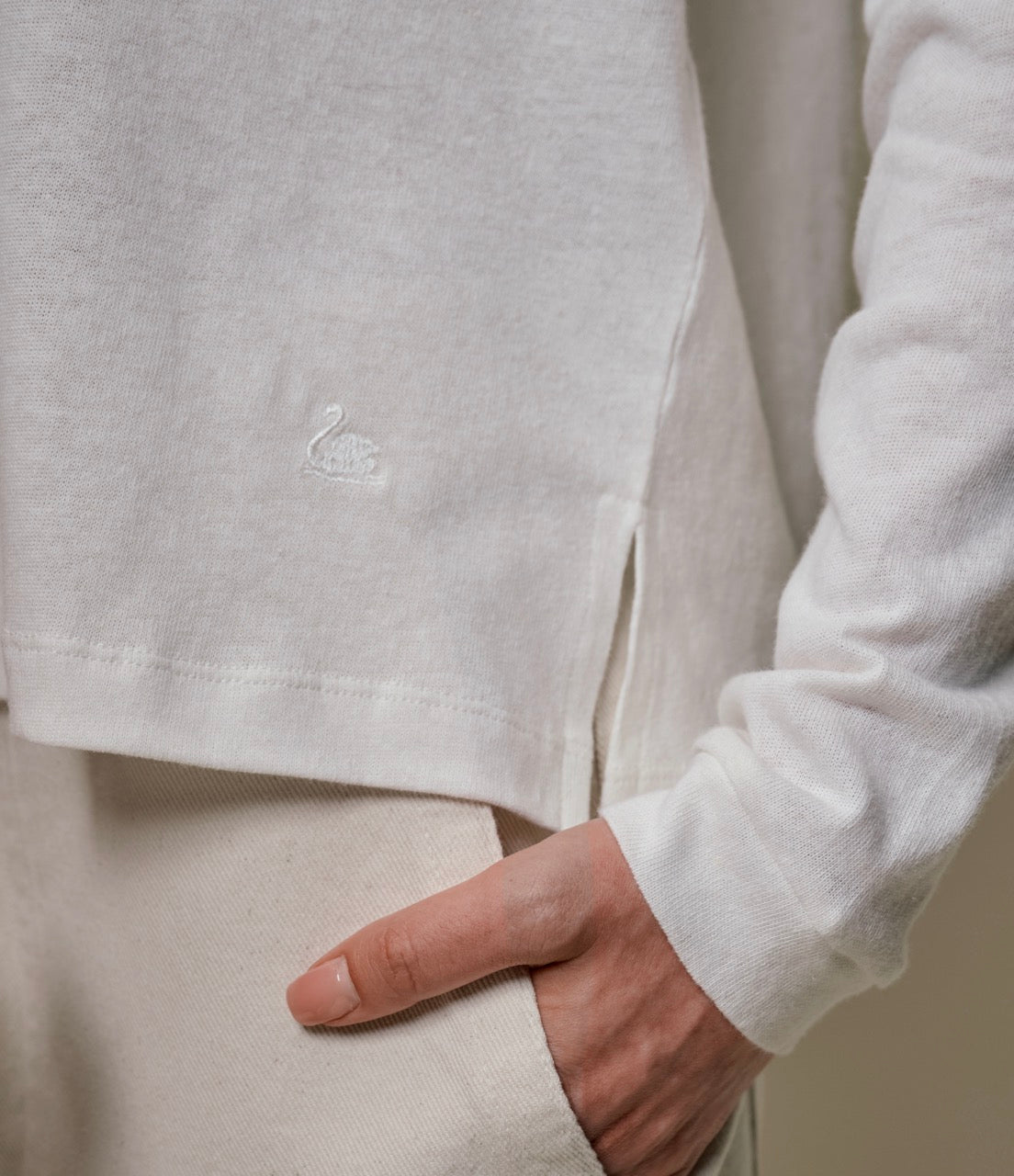 Close-up of a person wearing a white linen long-sleeve shirt with a swan logo on the chest.