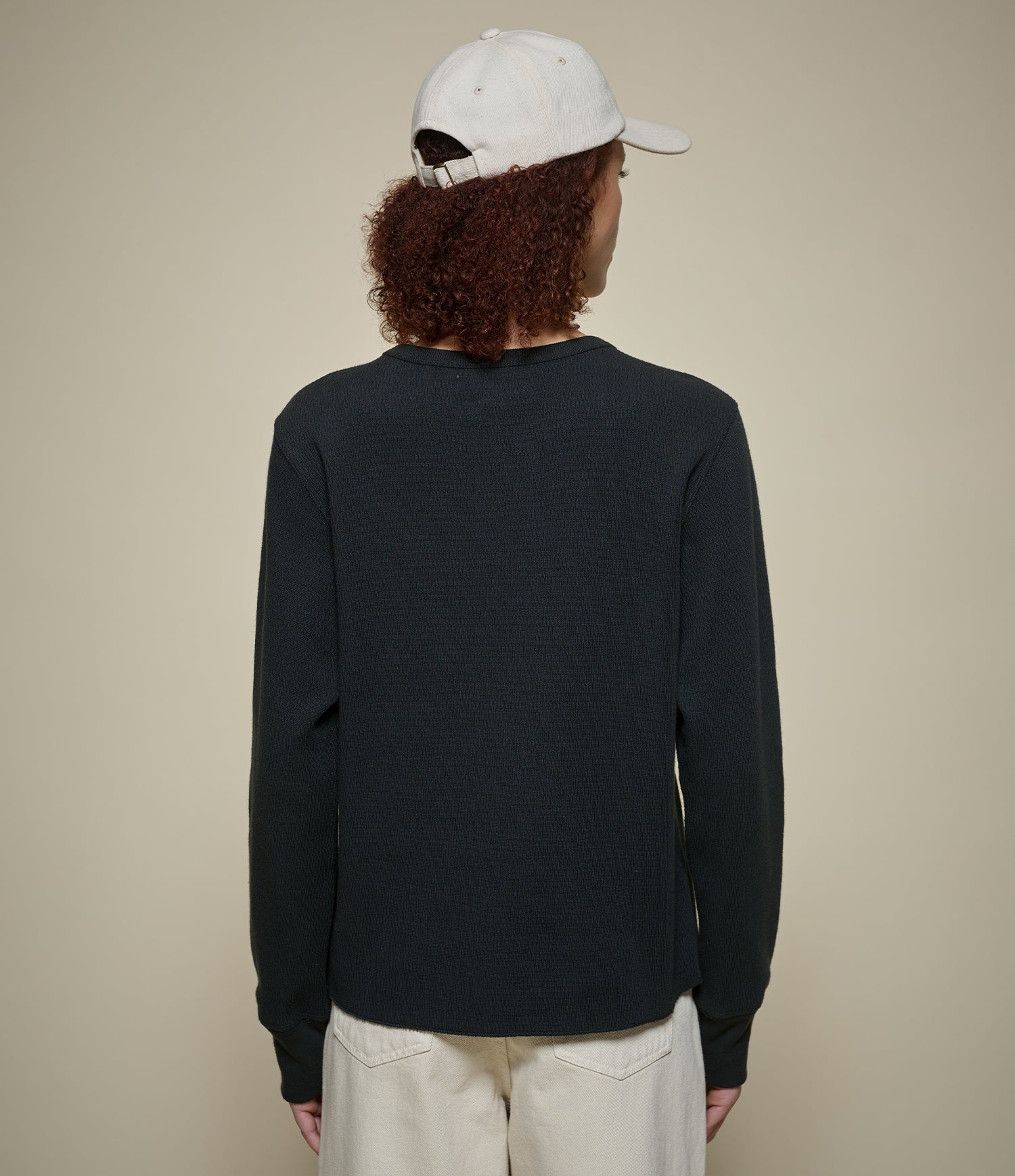 Person wearing a black longsleeve thermal shirt and white cap from behind on a beige background
