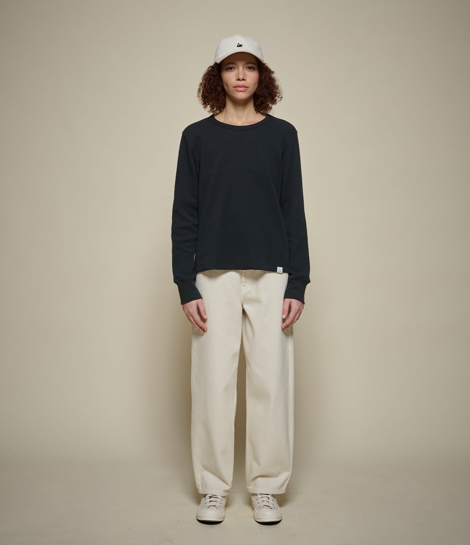 Person wearing a black thermal shirt, white pants, and a white cap on a beige background