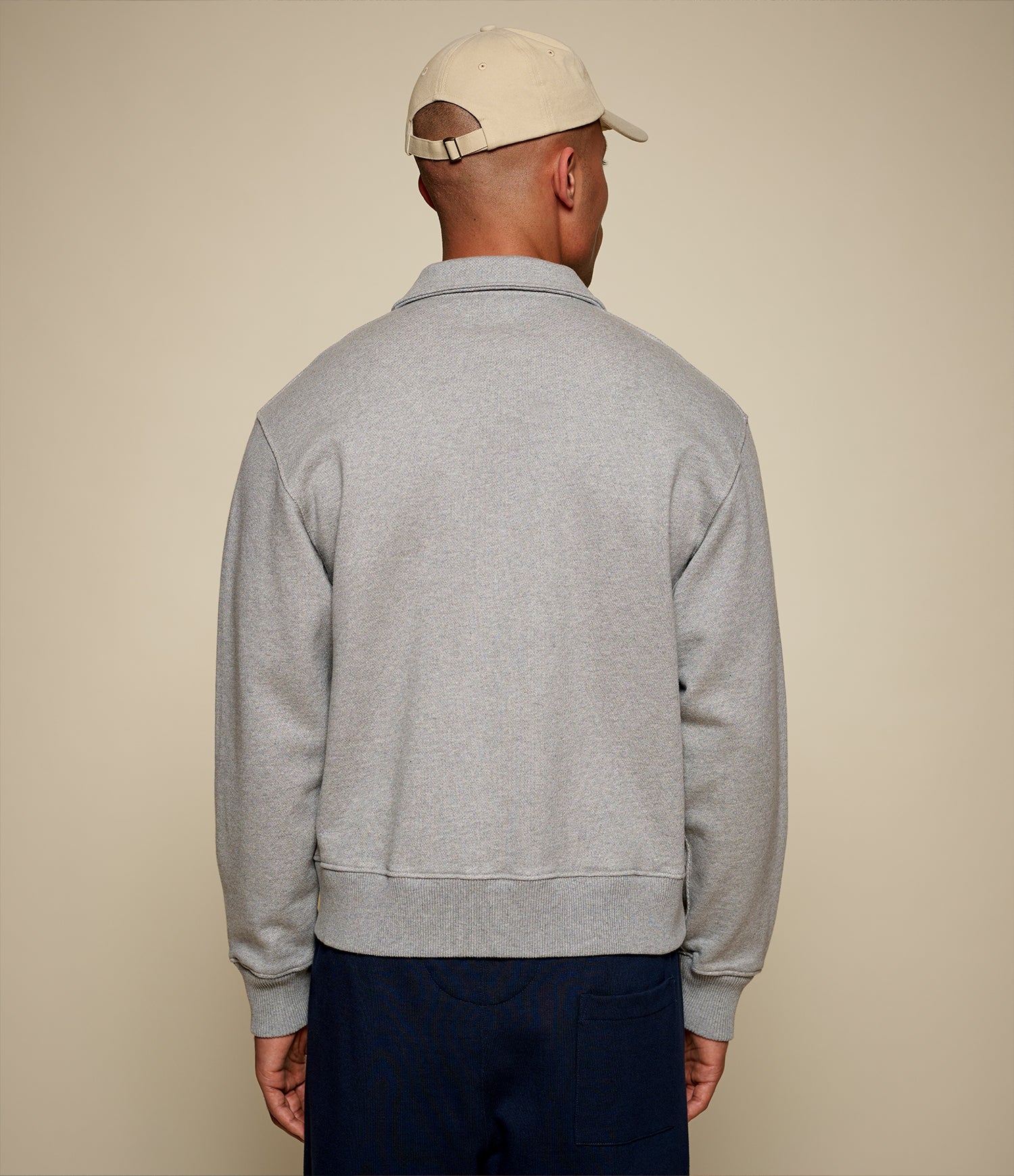 Man wearing a gray sweatshirt and beige cap from behind on a beige background